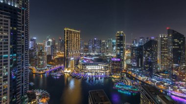 Dubai Marina hava saatinin gece aydınlanması, BAE. Modern gökdelenler ve konut binaları. Yollarda trafik vardı. Yapay kanal şehrindeki alışveriş merkezinin yakınındaki yatlar ve tekneler.
