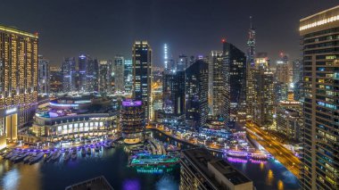 Dubai Marina 'nın gece aydınlatması panoramik zaman ayarlı, BAE. Modern gökdelenler ve konut binaları. Yollarda trafik vardı. Yapay kanal şehrindeki alışveriş merkezinin yakınındaki yatlar ve tekneler.