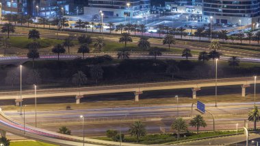 Büyük bir şehir gecesindeki yol kavşağının hava görüntüsü. BAE 'nin Dubai Marina bölgesinde arabaları, gökdelenleri ve tramvayları olan şehir manzarası.