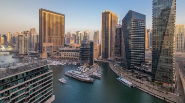 Gün batımında alışveriş merkezi olan Dubai marinası silueti. Kanalda yatları ve tekneleri olan çok uzun gökdelenler için harika bir bakış açısı. Binaların üzerinde güneş ışığı. Birleşik Arap Emirlikleri.