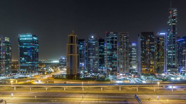 Jumeirah göl kuleleri, aydınlık gökdelenleri olan gece hava saatleri, Şeyh zayed yolu ve metro hattı trafiği. Dubai marinasından çatı manzarası