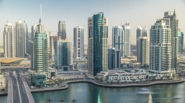 Gün batımında inanılmaz renkli Dubai marinası silueti. Rıhtımdaki en uzun gökdelenlerin, yatların ve teknelerin olduğu harika bir perspektif. Binaların üzerinde güneş ışığı. Birleşik Arap Emirlikleri.