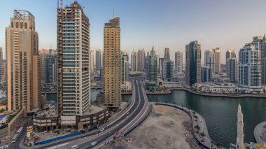 Dubai Marina gezinti güvertesi ve kanalı, gün batımından sonra Dubai, BAE 'de yüzen yatlar ve teknelerle hava üzerinden gece gündüz geçiş zamanı. Modern kuleler ve yol trafiği