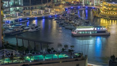 Dubai Marina 'daki gezinti güvertesi ve kanalı. Limanda yatları var. Zaman çizelgesi, Birleşik Arap Emirlikleri. Yürüyüş yolunda restoranları ve kafeleri olan hava manzaralı.