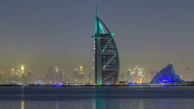 Palm Jumeirah timelapse hyperlapse üzerinden Burj Al Arab ile gece manzarası Dubai. Suya yansıyan ışıklandırılmış gökdelenler