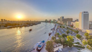 Dubai creek manzara tekneler ve yatlar ile günbatımı timelapse ve trafik yol ve otopark ile modern binalar. Yukarıdan hava üstten görünüm