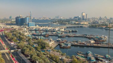 Dubai deresi zaman çizelgesi, limanda tekne ve gemi, sakin su ve günbatımında modern binalar. Yukarıdan yol boyunca trafik ve ağaçlarla hava manzarası