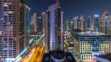Dubai Marina 'nın hava panoramik görüntüsü gece görüş mesafesinden. Parlayan pencerelerle aydınlatılmış modern gökdelenler ve konut kuleleri. Yolda trafik vardı.
