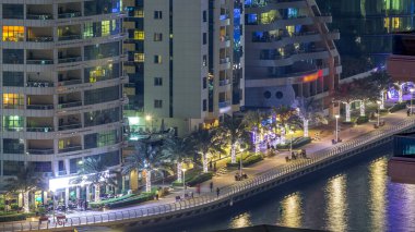 Dubai Marina havadan görünümden bir noktadan gece timelapse. Waterfront adlı mesire üzerinde yürüyen insanlar. Modern gökdelenler ve konut kuleleri parlayan pencerelerle aydınlatılmış