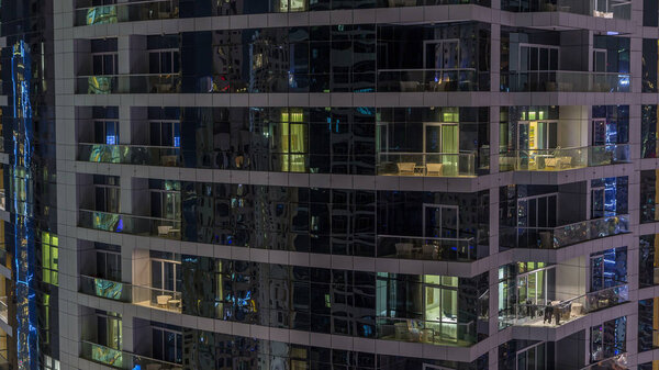 Glowing windows of skyscrapers at evening timelapse. View of modern residential high-rise buildings in Dubai marina. People moving inside apartments. Aerial top view.