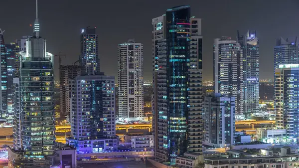 Residential towers with lighting and illumination timelapse. Road and promenade on Dubai Marina and JLT skyline at night. Traffic near skyscrapers with glowing windows