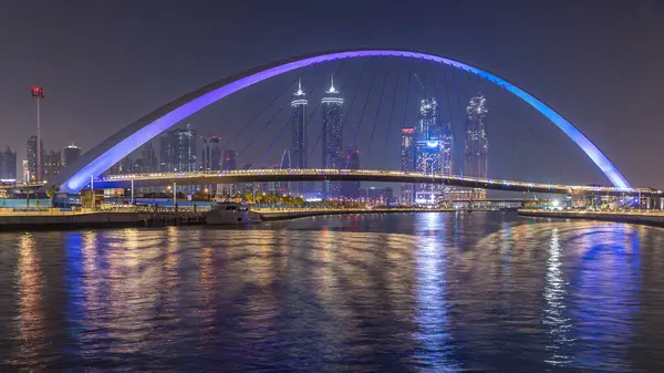 Futuristic Pedestrian Bridge over the Dubai Water Canal Illuminated at Night timelapse, UAE. Cityscape on background. View from promenade