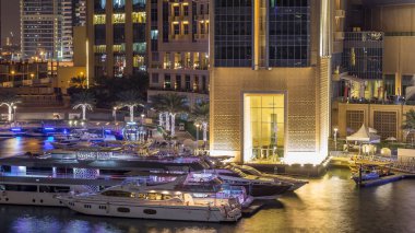 Dubai Marina 'nın hava görüntüsü, alışveriş merkezi, restoranlar, kuleler ve yatlar, Birleşik Arap Emirlikleri. Aydınlatılmış binalar ve liman manzaralı bir kanal.