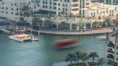 Lüks Dubai Marina kanalı kıyısı, oradan geçen tekneler ve palmiyelerle dolu bir gezinti, akşam olmadan yukarıdan manzaralı. Dubai, Birleşik Arap Emirlikleri