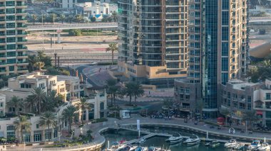 Lüks Dubai Marina Kanalı 'ndan geçen tekneler, yatlar ve palmiyeli gezinti güvertesi, akşamdan önce yukarıdan bir manzara. Dubai, Birleşik Arap Emirlikleri