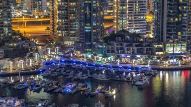 Lüks Dubai Marina Kanalı 'ndan geçen tekneler, yatlar ve restoranlarla dolu bir gezinti yeri gece zaman çizelgesi, yukarıdan aydınlık gökdelenleri olan bir manzara. Dubai, Birleşik Arap Emirlikleri