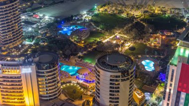 Modern ışıklandırılmış gökdelenler ve Jumeirah Beach Residence (Jbr) gece timelapse Dubai, BAE kumsalda hava görünümünü. Yeşil çim ve havuzları
