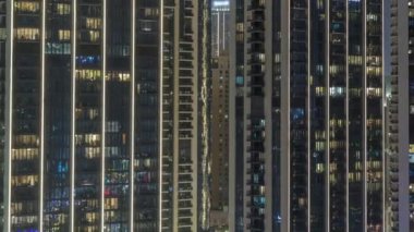 Şehrin hava zaman ayarlı yerleşim bölgesinde parlayan pencereleri olan uzun apartmanlar. Kulelerdeki dairelerin odalarında akşam ışığı ve aydınlatılmış gökdelenler