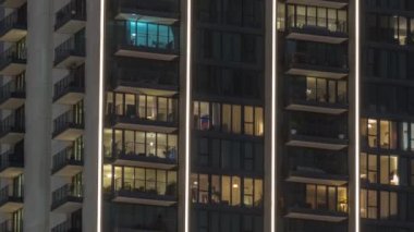 Şehrin hava zaman ayarlı yerleşim bölgesinde parlayan pencereleri olan uzun apartmanlar. Kulelerin ve gökdelenlerin tepesindeki odalarda akşam ışığı