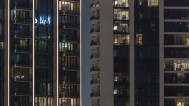 Kulelerdeki ve gökdelenlerdeki odalarda akşam ışığı. Şehrin yerleşim bölgesinde parlayan pencereleri olan uzun apartman blokları..