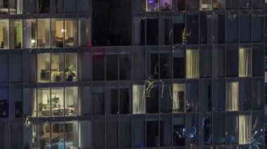 Apartman binasının ön cephesinde ışık zamanlaması olan bir sürü parlak pencere var. Her pencerede hayat var. Yerleşim yeri gökdelenin cam cephesinin havadan görünüşü.