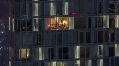 Kule binasının gece ön cephesinde ışık zamanlaması olan apartmanların bir sürü penceresi var. Her pencerede hayat var. Ofisin cam cephesinin ve yerleşim yerinin hava görüntüsü..