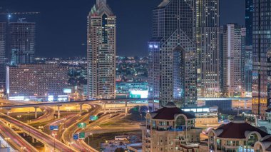 Dubai gece timelapse ışıklı gökdelenler ve yol kavşağı havadan görünümü. Etrafında modern kuleleri ile şehir merkezinde kavşakta Trafik. Bulutlu gökyüzü