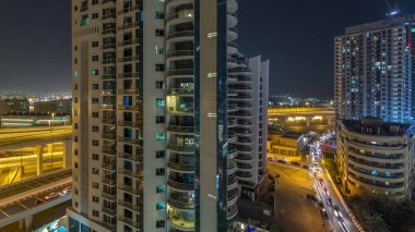 Dubai Marina 'da aydınlık gökdelenler ve gezinti güvertesi gece saatleri. Yol trafiği olan modern kuleler ve tekneler. Birleşik Arap Emirlikleri