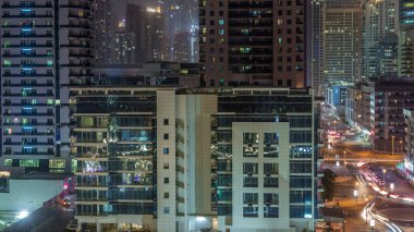 Dubai Marina 'da aydınlık gökdelenler ve gezinti güvertesi gece saatleri. Yol trafiği olan modern kuleler ve tekneler. Birleşik Arap Emirlikleri