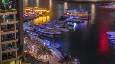 Dubai Marina körfezindeki iskeleye park etmiş lüks yatlar. Şehir hava manzaralı gece manzaralı. Etrafında kuleler ve gökdelenler olan gezinti yolu