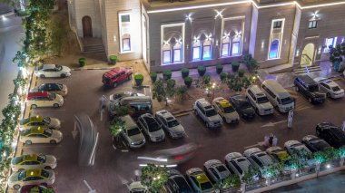 Dubai Marina 'daki Al Rahim Camii' nin yakınındaki otoparklarda hareket halindeki arabalar gökdelenler arasındaki aydınlık dini bina.