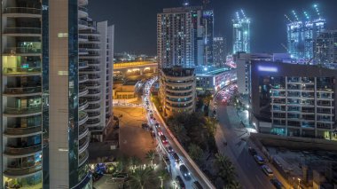 Dubai Marina 'da aydınlık gökdelenler ve gezinti güvertesi gece saatleri. Yol trafiği olan modern kuleler ve tekneler. Birleşik Arap Emirlikleri