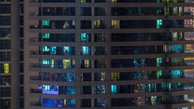 Geceleri apartmanın iç kısımlarında insanlar olan parlak pencereler. Camdan yüzeyi olan modern bir gökdelen. İş ve modern hayat kavramı