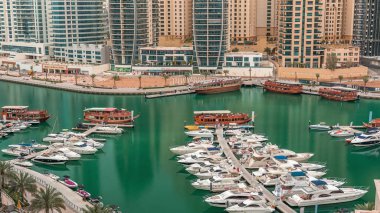 Dubai Marina körfezindeki iskeleye park etmiş lüks yatlar. Şehir hava manzaralı zaman ayarlı. Sabah erken saatlerde kuleler ve gökdelenler