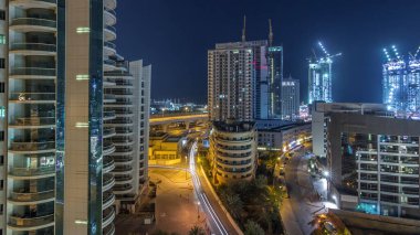 Dubai Marina 'da aydınlık gökdelenler ve gece gündüz gezinti güvertesi geçiş zamanı. Yol trafiği olan modern kuleler ve tekneler. Birleşik Arap Emirlikleri