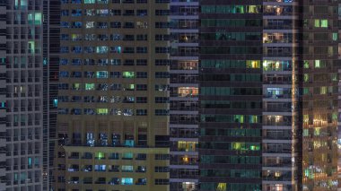 Geceleri apartmanların iç kısımlarında insanlar olan parlak pencereler. Camdan yüzeyi olan modern gökdelenler. İş ve modern hayat kavramı