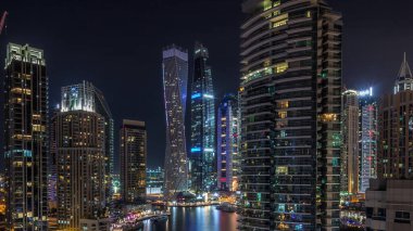 Dubai Marina konutlarının ve ofis gökdelenlerinin panoramik hava manzarası ve tüm gece boyunca deniz kenarında yanıp sönen ışıklar. Yüzen tekneler ve yatlar