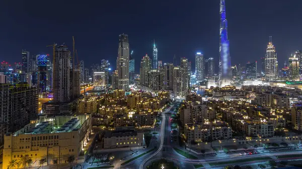 Dubai Downtown skyline during all night timelapse with Burj Khalifa and other towers panoramic view from the top in Dubai, United Arab Emirates. Moon on the sky. Traditional and modern buildings.