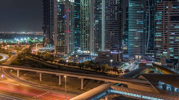 Dubai Marina 'dan Şeyh Zayed yoluna giden hava görüntüsü. Dubai' deki gökdelenlerin aydınlatıldığı gece zaman çizelgesi. Trafik, yaya köprüsü ve metro hattı. Birleşik Arap Emirlikleri