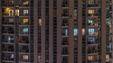 Geceleri apartmanın iç kısımlarında insanlar olan parlak pencereler. Şehirde modern bir gökdelen. İş ve modern hayat kavramı