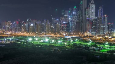 Dubai Marina, Dubai, Birleşik Arap Emirlikleri'nde gece saatlerinde gökdelenleri ve golf sahalarını aydınlatmaktadır. Yeşiller bölgesinden havadan görünüm