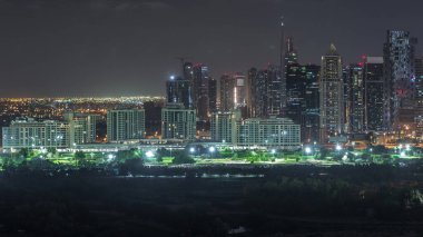 Jumeirah lake towers illuminated skyscrapers and golf course night timelapse, Dubai, United Arab Emirates. Aerial view from Greens district clipart