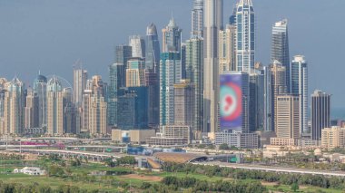 Dubai Marina tallest skyscrapers and golf course morning timelapse, Dubai, United Arab Emirates. Aerial view from Greens district. Green lawn and cloudy sky clipart