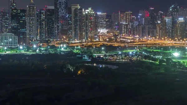 ジュメイラ湖の塔とドバイマリーナ照明超高層ビルやゴルフコースの夜のタイムラプス ドバイ アラブ首長国連邦 グリーンズ地区からの航空写真 — ストック写真