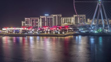Dubai'deki Bluewaters Adası'nda ışıklı binalarla gece saati. Yatlar ve tekneler geçiyor. Jumeirah Beach Residence kıyılarında bulunan insan yapımı ada