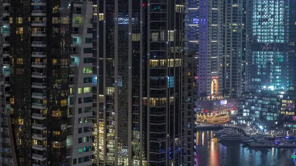 Dubai Marina konutlarının ve ofis gökdelenlerinin pencerelerinde ışıklar ve deniz kıyısında gece saatleri olan hava manzarası. Yüzen tekneler ve yatlar