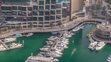 Dubai marina timelapse yüzen yatlar üzerinde havadan görünümü. Beyaz tekneler yeşil kanal suyunda. Mağaza ve restoranlar ile gezinti.