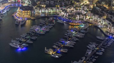 Dubai marina gece zaman atlamalı yüzen yatlar havadan görünümü. Beyaz tekneler kanal suyunda. Mağazalar ve restoranlar ile Aydınlatılmış gezinti.