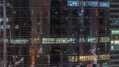 Ofis gökdeleni gece geç saatlerde iç ışıklar açıkken ve insanlar gece vardiyasında çalışırken. Yukarıdan birçok pencereye sahip havadan yakın görüntü