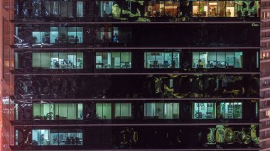 Ofis gökdeleni gece geç saatlerde iç ışıklar açıkken ve insanlar gece vardiyasında çalışırken. Yukarıdan birçok pencereye sahip havadan yakın görüntü